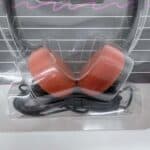 Over-ear earmuff-style headphones with red cushions in plastic packaging with wired connector attached